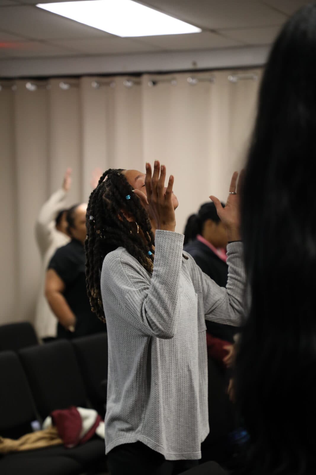 A woman worshipping with both hands lifted and eyes closed