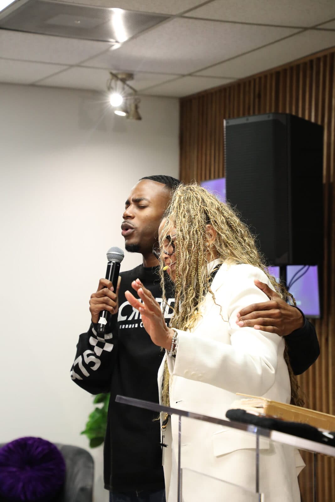 A man ministering on the microphone with his arm around a member during service