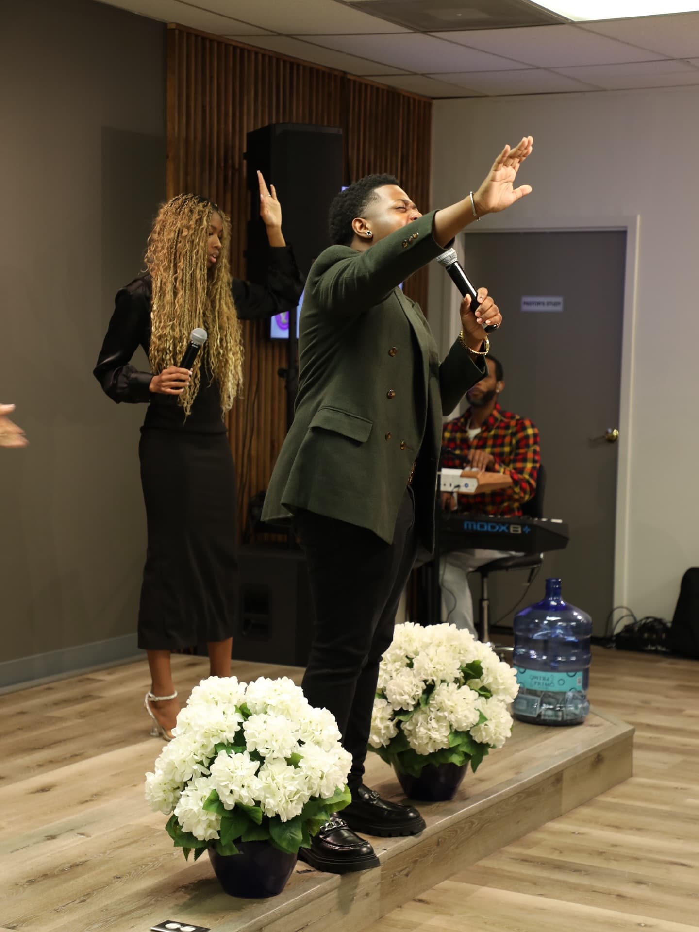 A worship leader singing with one hand lifted while the band plays behind him